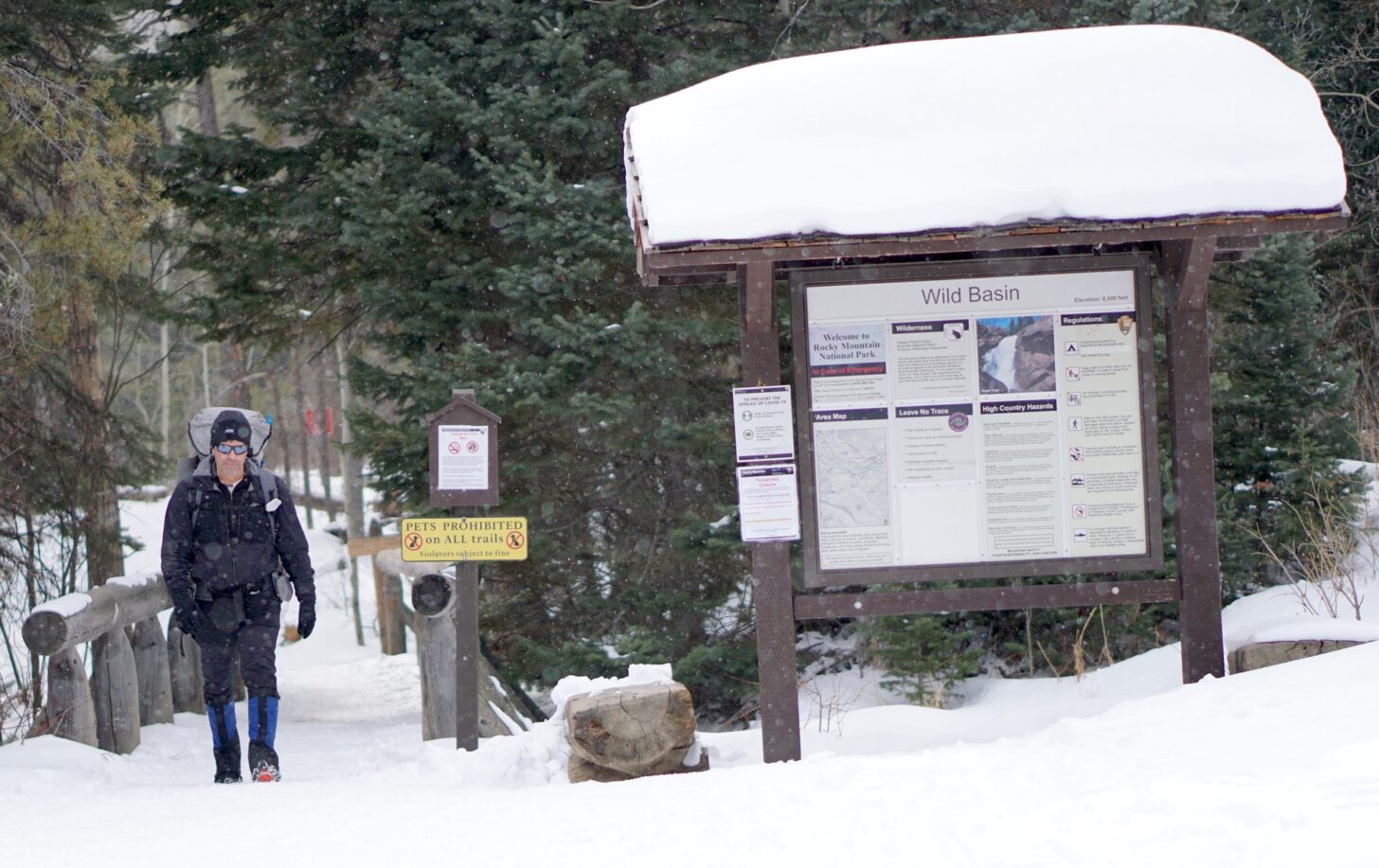 man hiking on bridge next to sign that reads "wild basin"