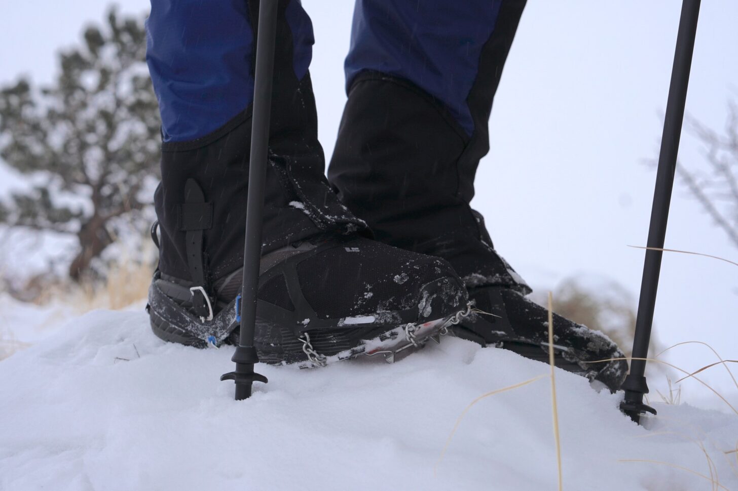 lower legs of a hiker wearing boots and gaiters, with traction spikes affixed to the boots; and trekking poles