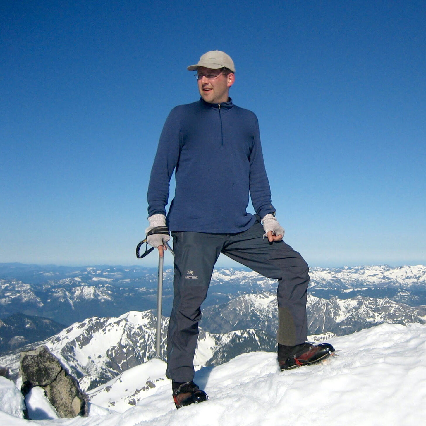 a man stands on a mountain peak with mountains in the background.