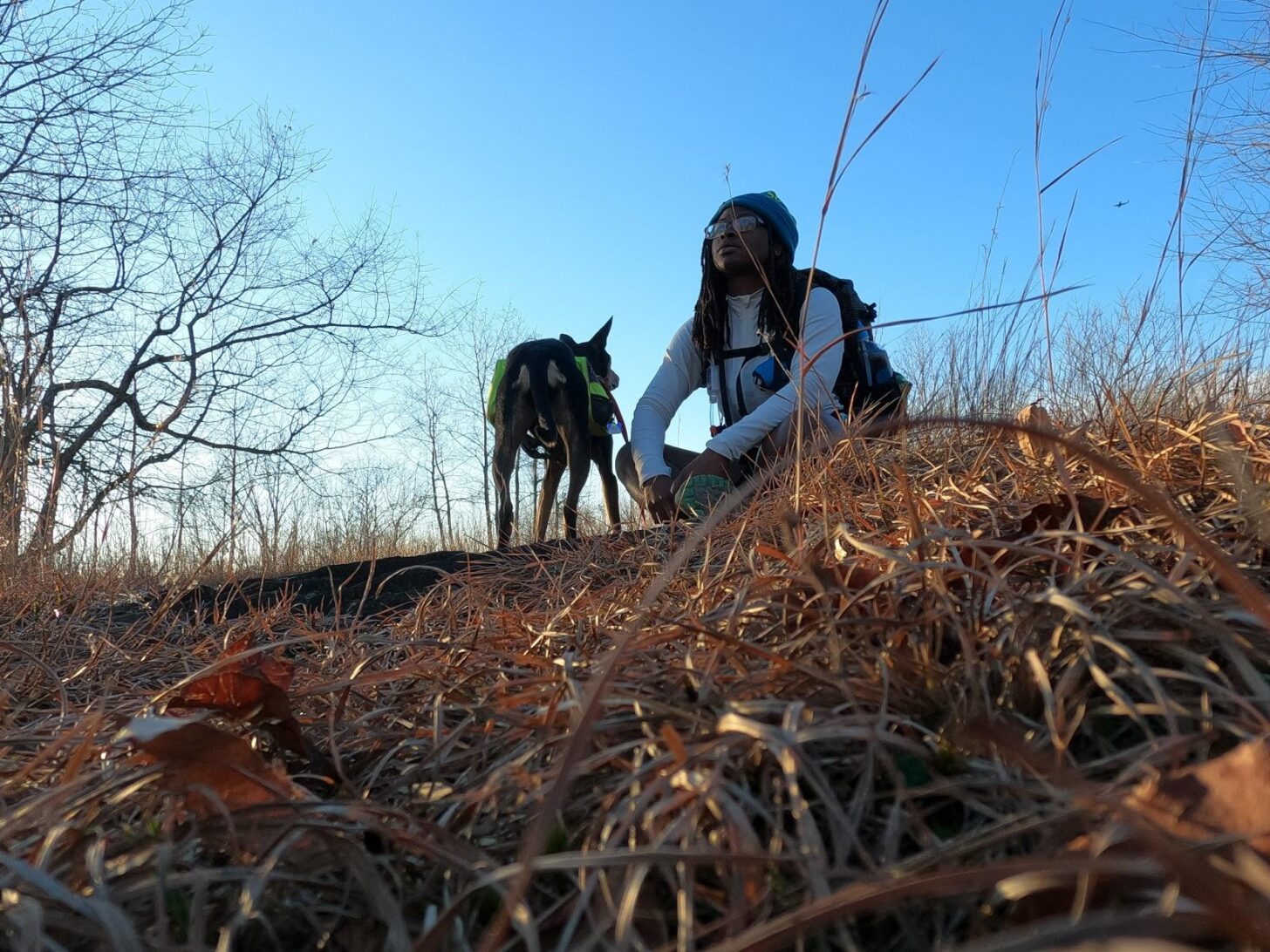 A Black woman and her dog resting in a field.