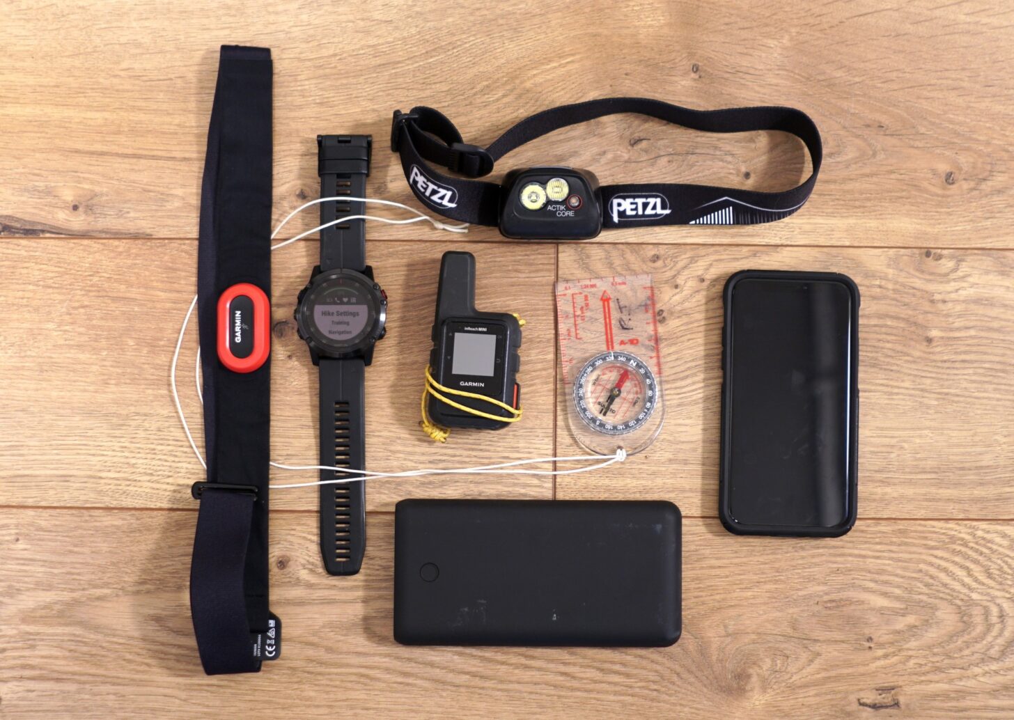 layout of navigation and electronics gear for winter backpacking - a heart rate monitor and fitness watch, satellite communicator, headlamp, compass, smartphone, and power bank