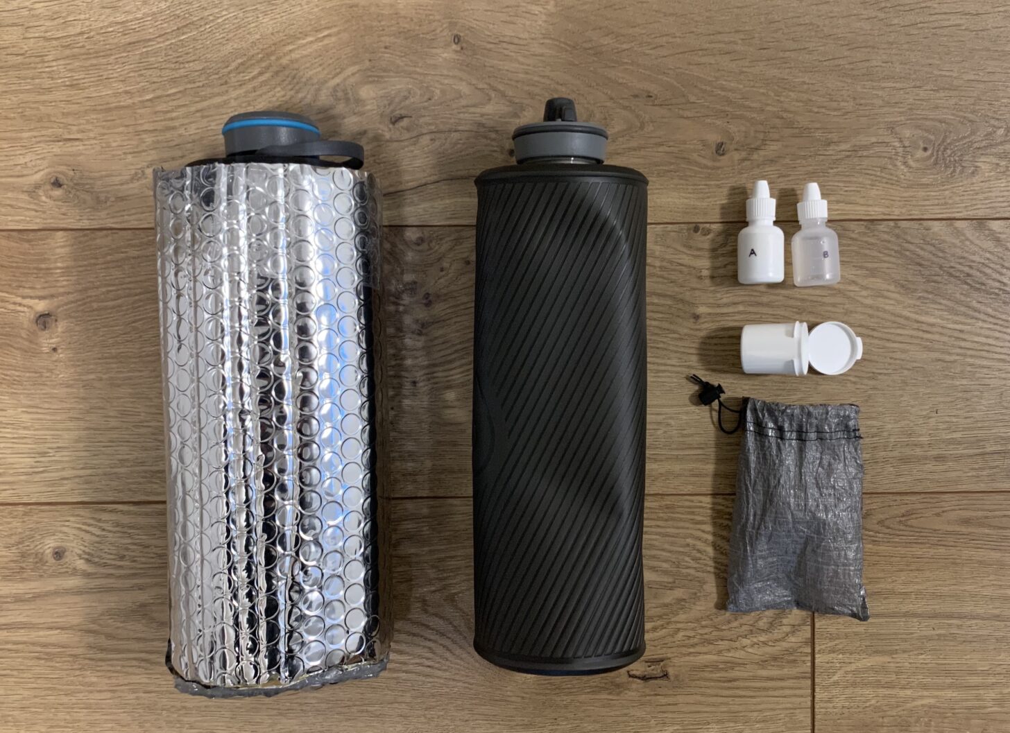 layout of hydration gear - a water bottle in a homemade reflective bubble wrap cozy, another water bottle, and a small aqua mira kit.
