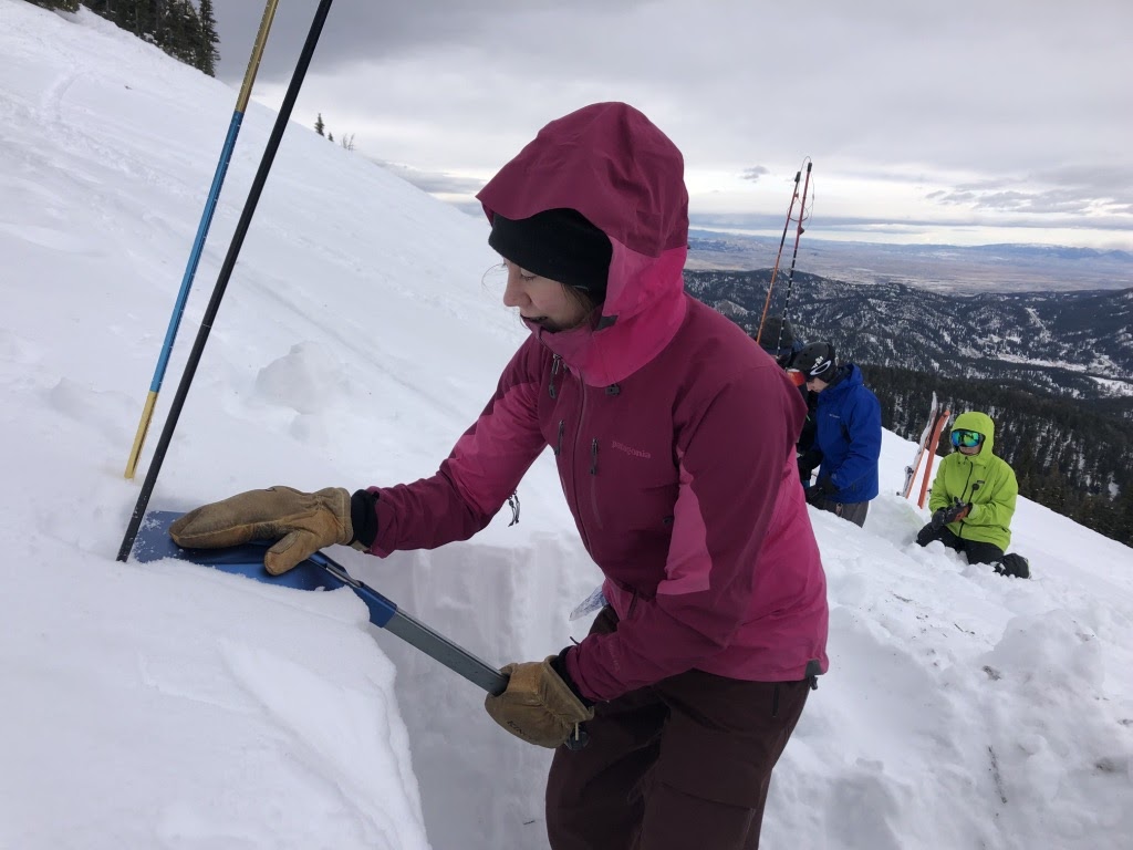 a woman digs a hole in the snow on a steep mountainside