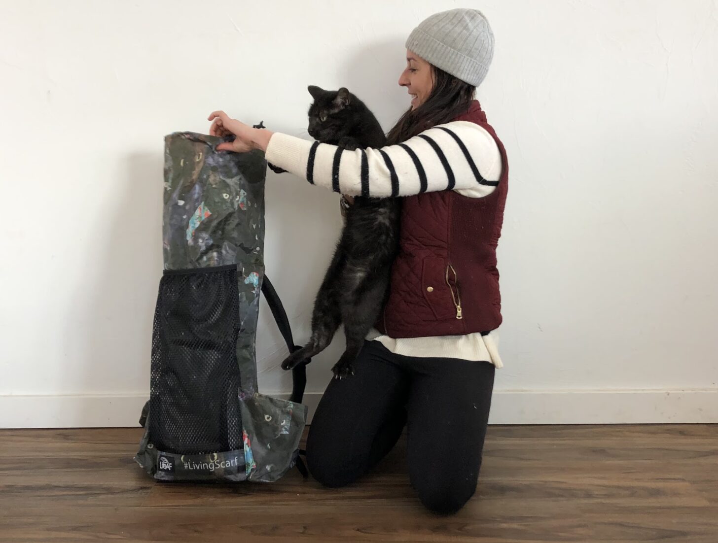 a woman trying to stuff a cat into a backpack