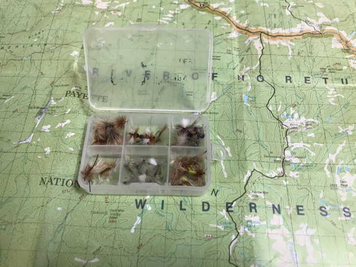 A fly box laid out against a map.