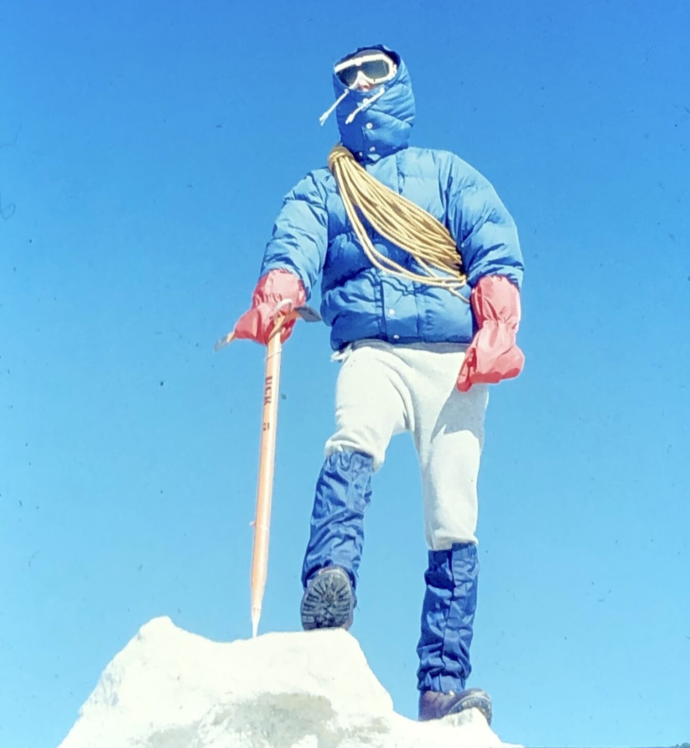 a man wearing a lot of gear stands on top of a mountain