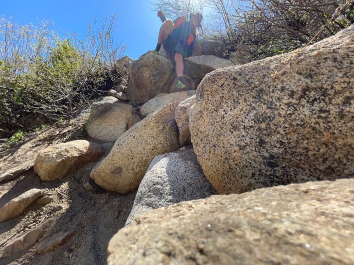 a man picks his way down a rocky slope while wearing an orange backpack.