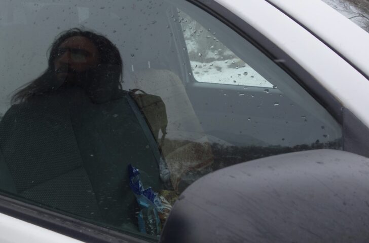 a man looks at his own reflection in a car window