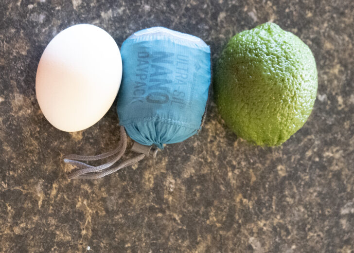a close up of three items of similar size - a white chicken egg, the compressed backpack, and a large lime.