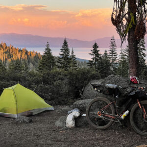 a bicycle and tent perched above a sunset