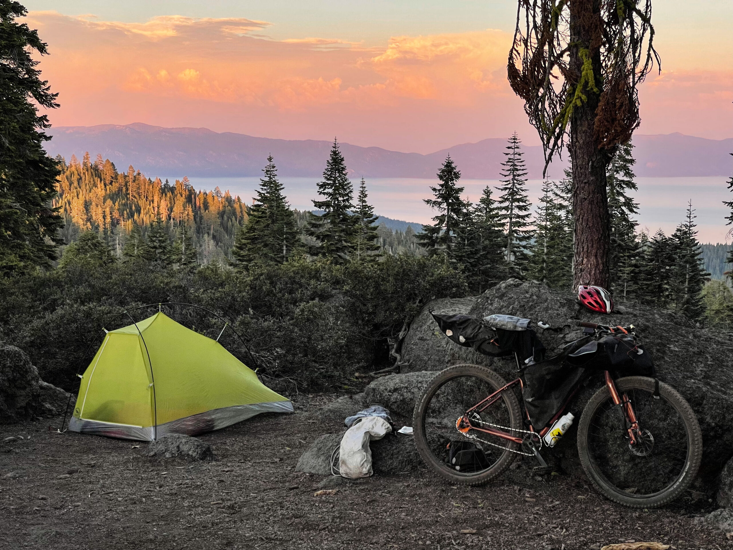 a bicycle and tent perched above a sunset