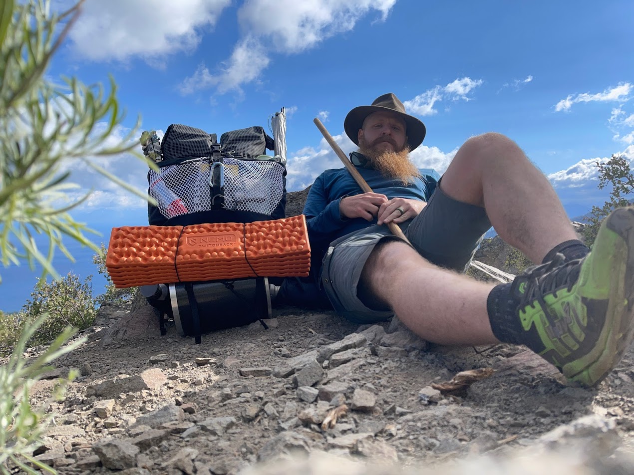 a man with a luscious red beard rests next to a fully loaded backpack.