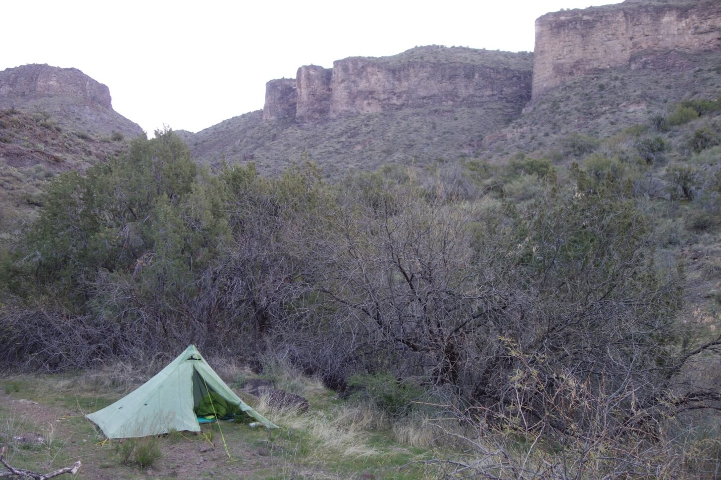 A pyramid style tent nestles into a hollow at the base of some cliffs.