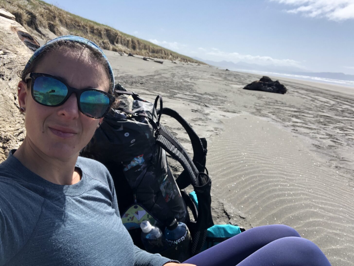 A woman rests next to her backpack with a beach scene in the background.