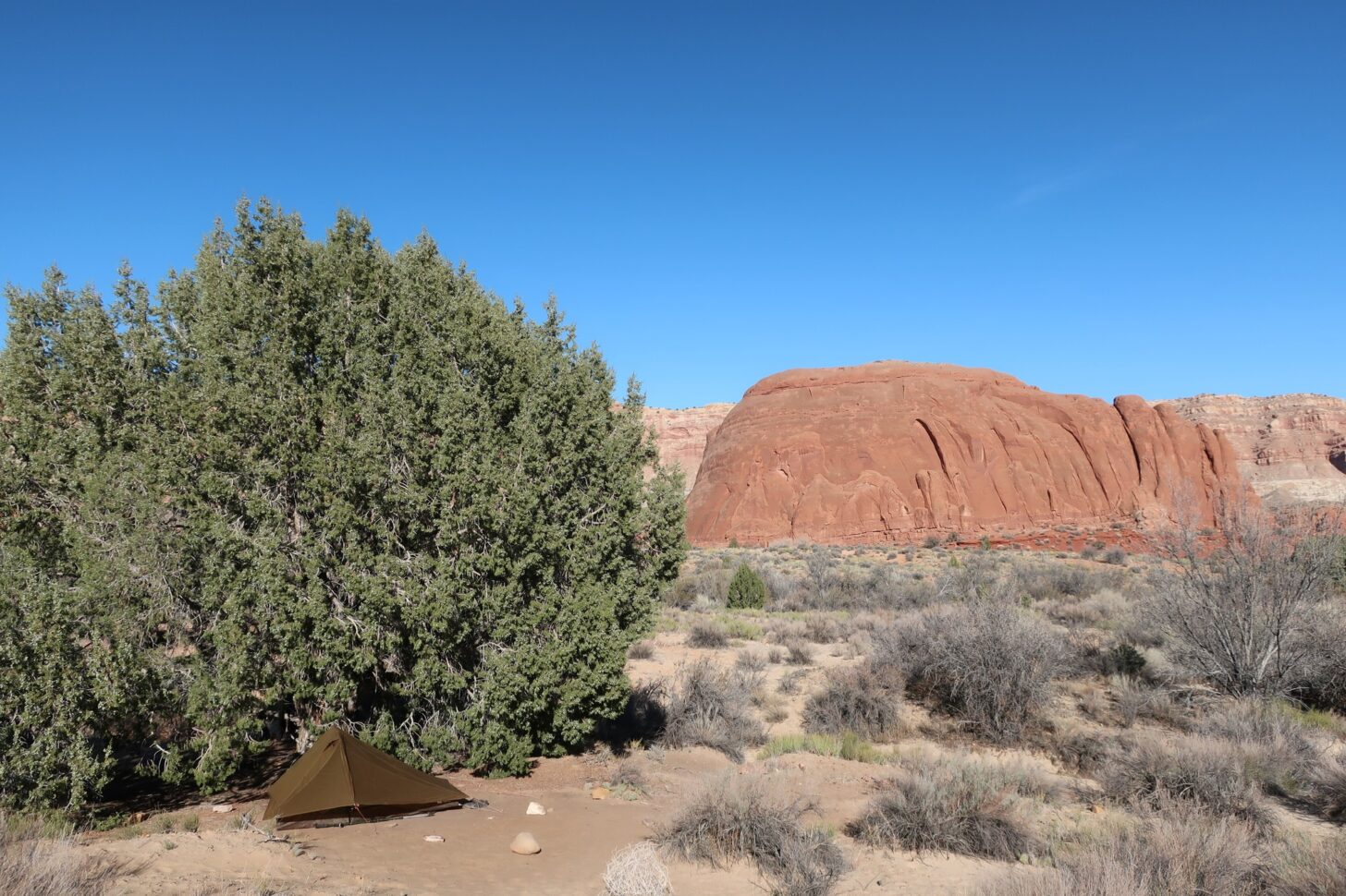 a flat campsite under a blue sky with red sandstone rocks in the background