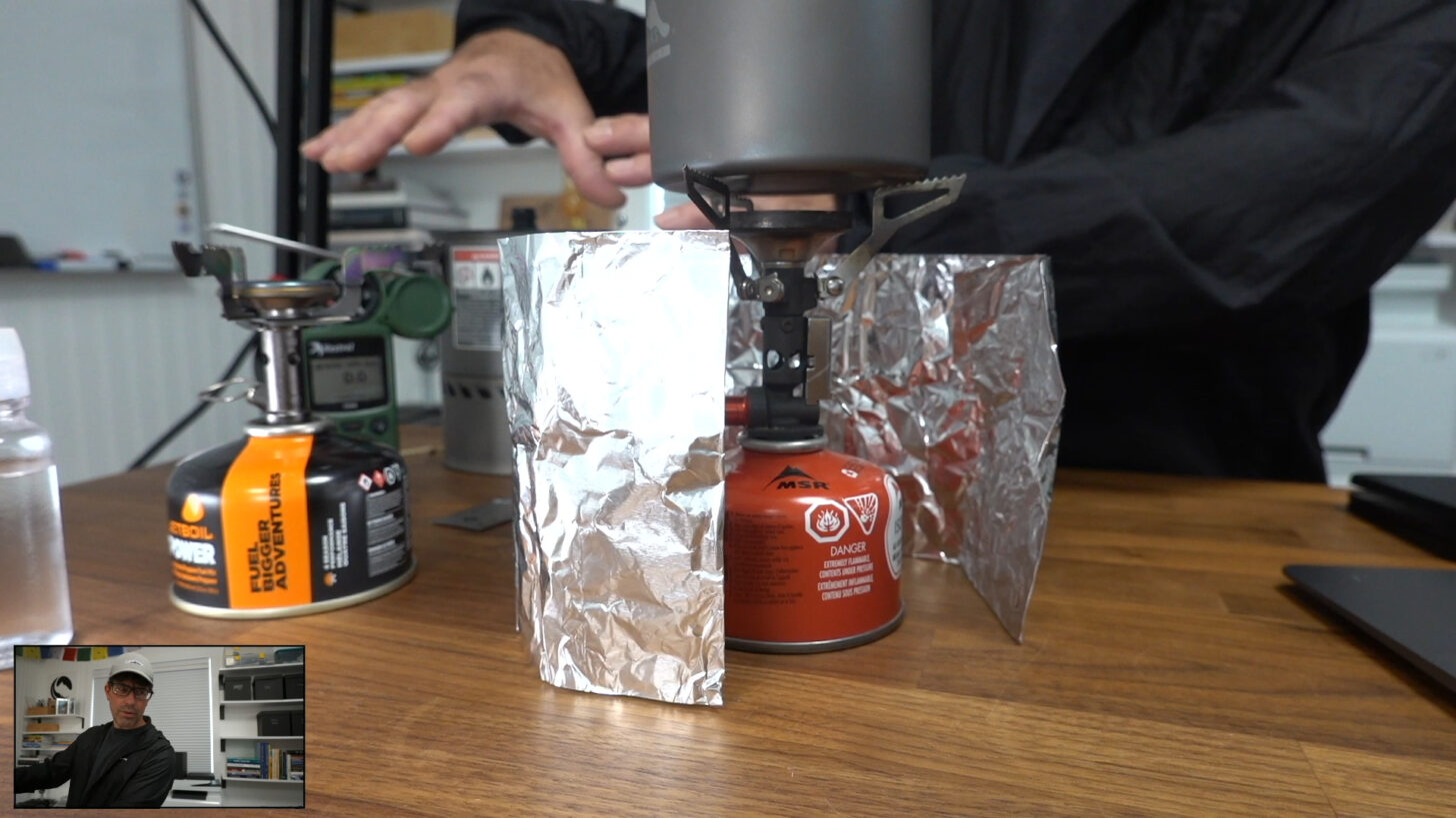 an upright canister stove surrounded by a cheap aluminum foil windscreen