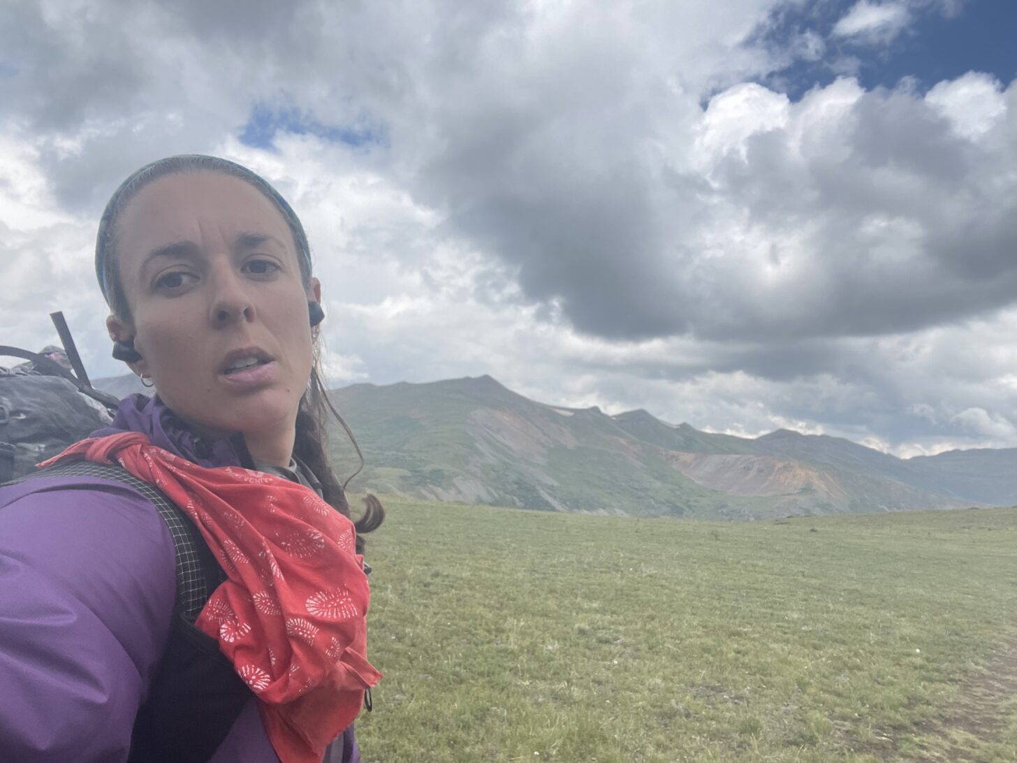 a woman makes a face at the camera while taking a selfie. Mountains in the background.