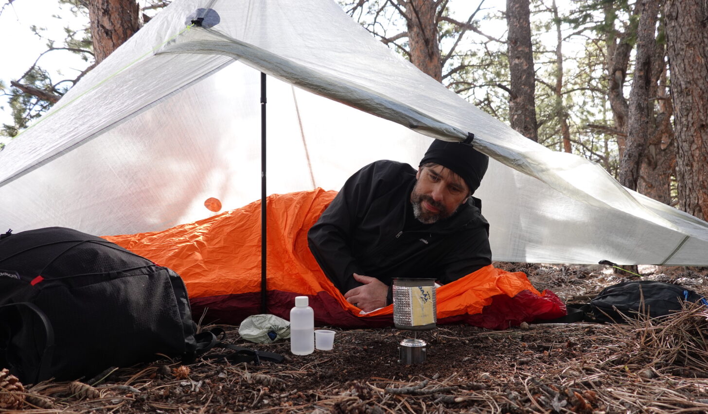 hiker under a shelter using an alcohol stove