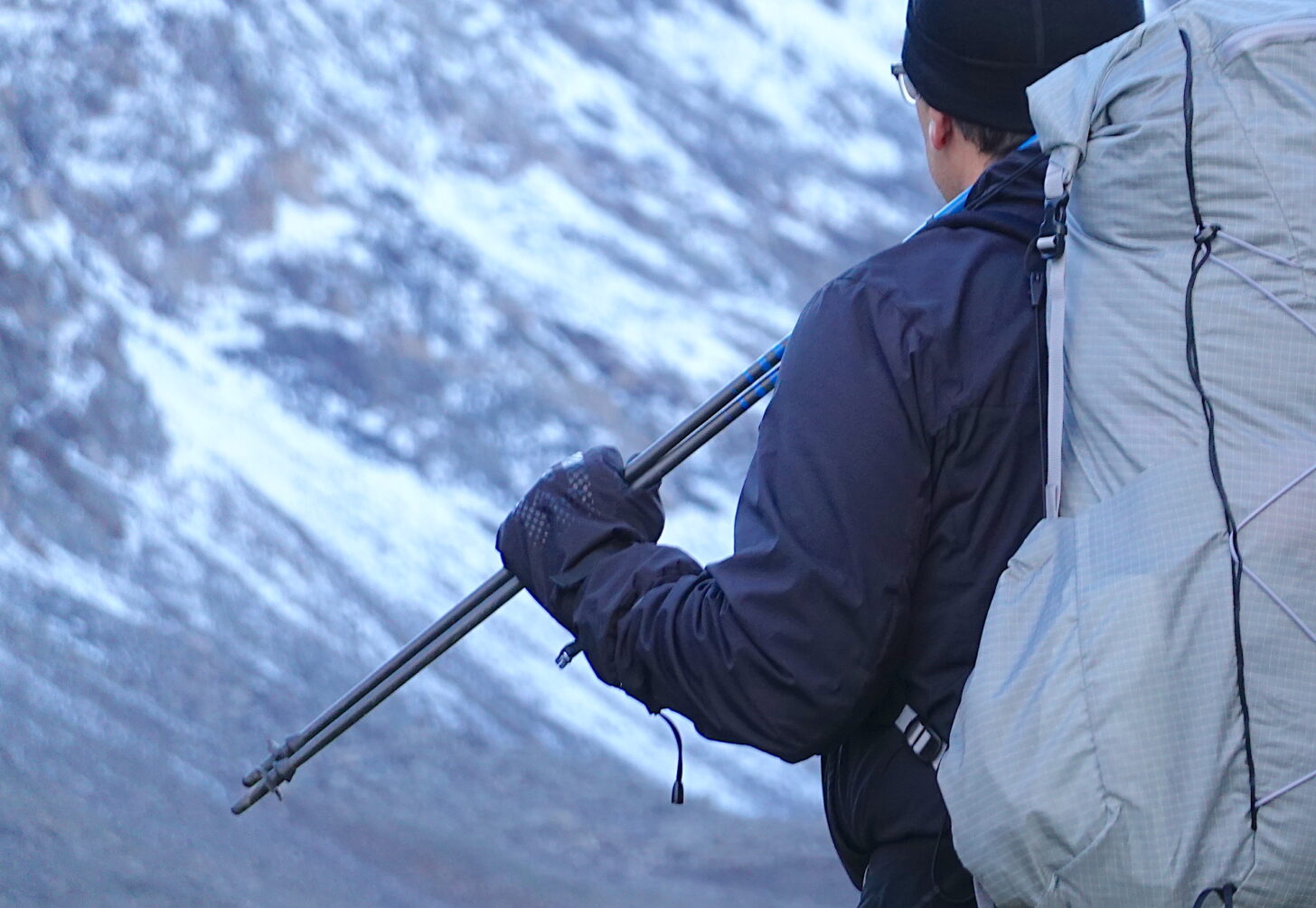 hiker in the mountains carrying a pack and holding trekking poles, wearing rain mitts