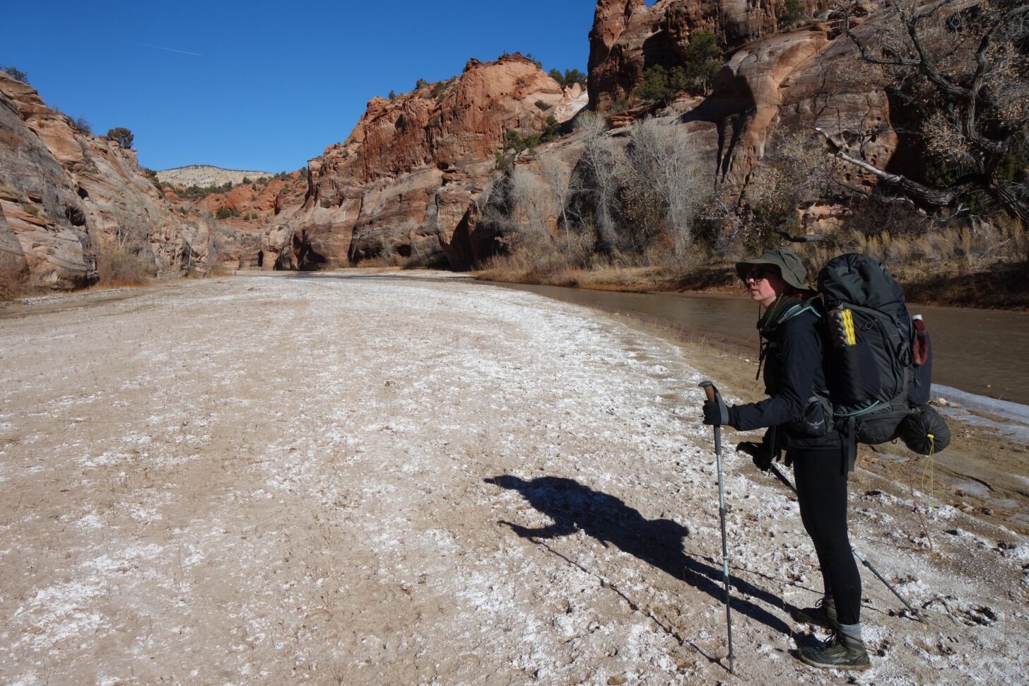 a woman stands on a frosted riverbank in a desert canyon