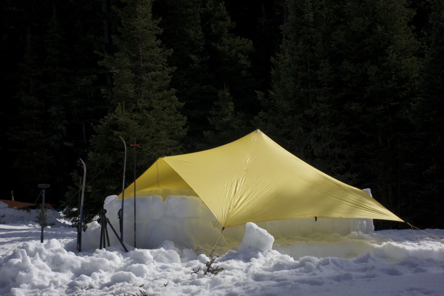 camping tarp pitched over a snowpit protected by snow block walls