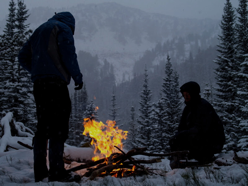 two hikers enjoying a campfire in snowy mountains