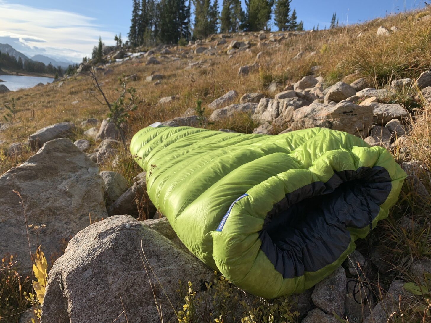 sleeping bag lying on a meadow with an alpine lake in the background