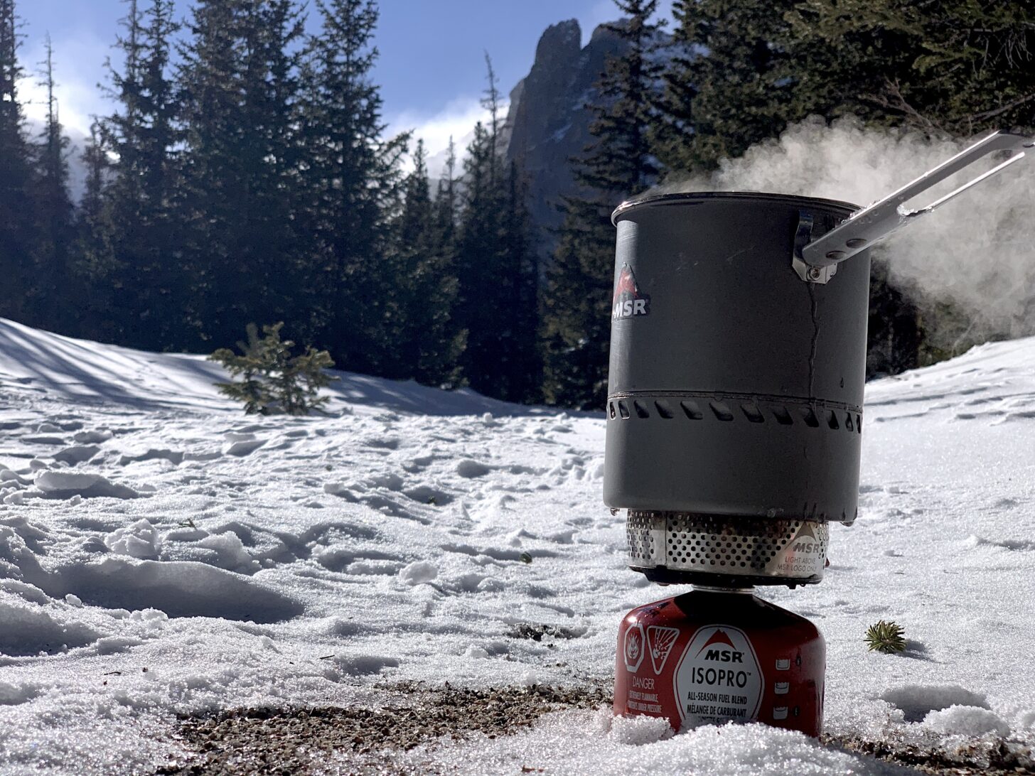 backpacking stove boiling water, snow on ground, mountains in the background