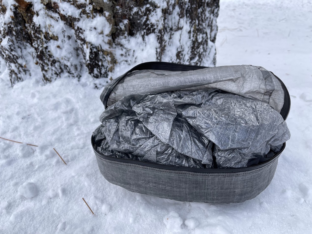 a hyperlight mountain gear pod sitting in the snow with a shelter packed in it.