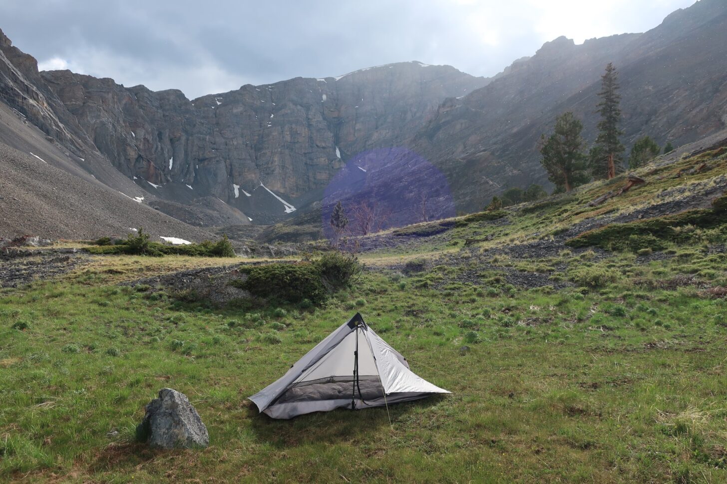A tent is in a meadow with mountains in the background
