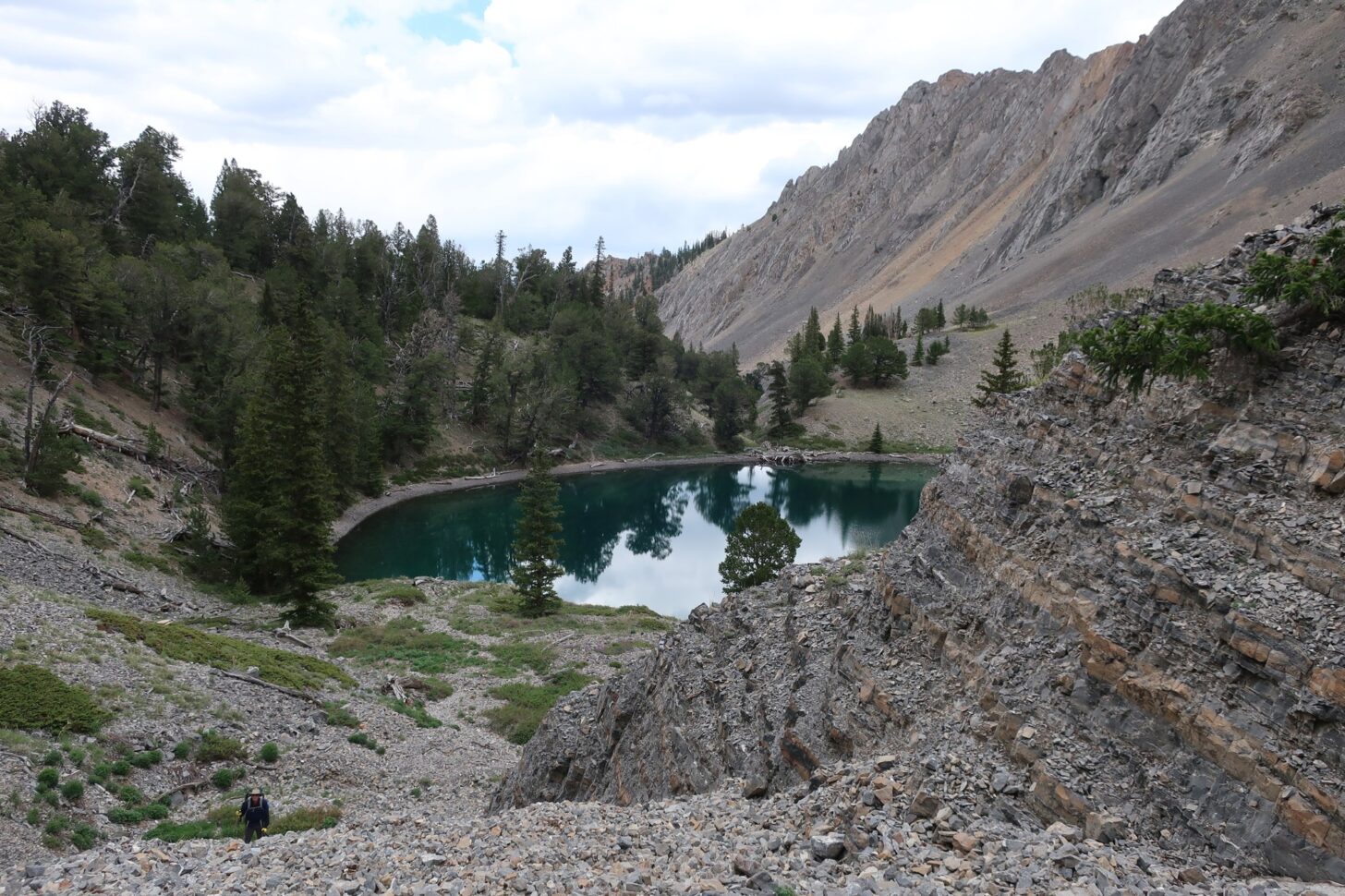 A hiker is shown hiking near a lake with mountains and forest in the background