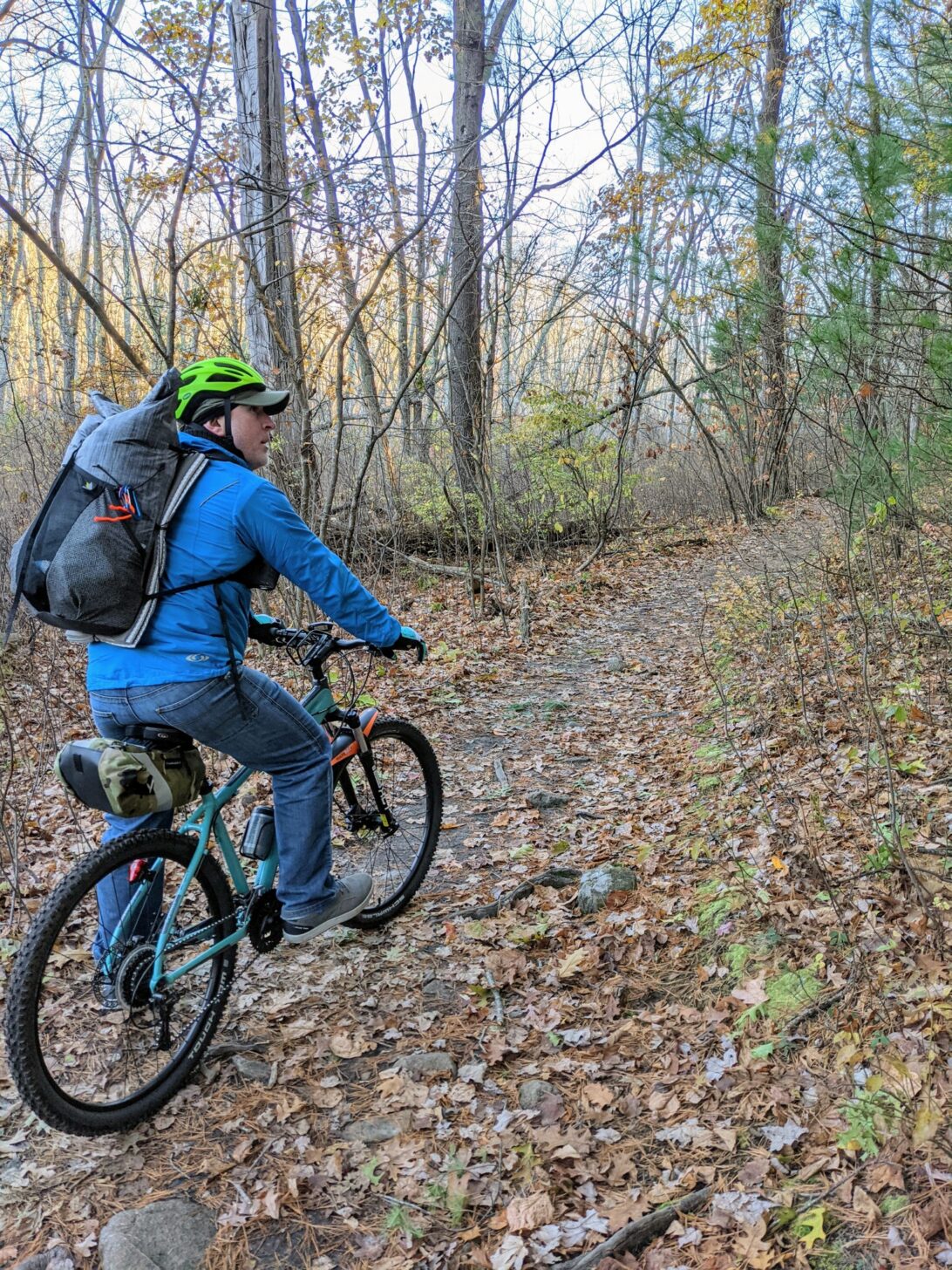 a man rides a bicycle while wearing the Nashville Pack Cutaway backpack.