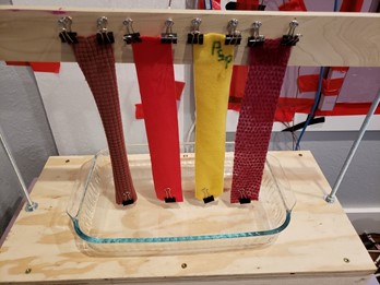 four strips of fabric suspended above a pan of water