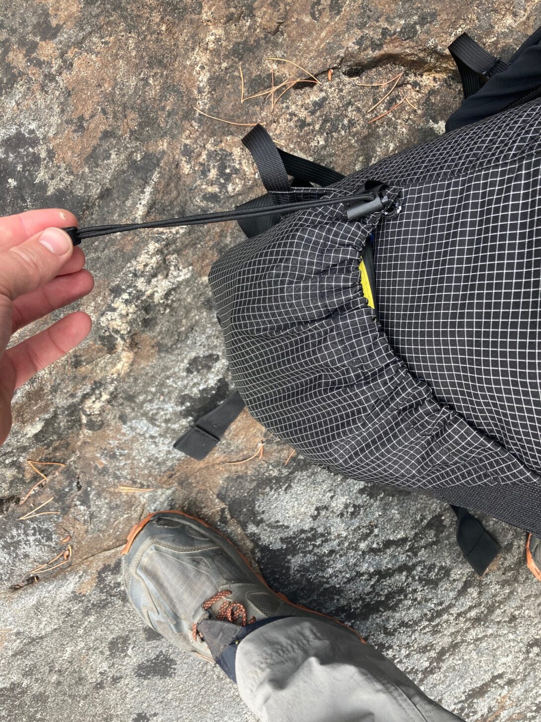 The side pocket of a backpack is shown being cinched tight by a drawstring.