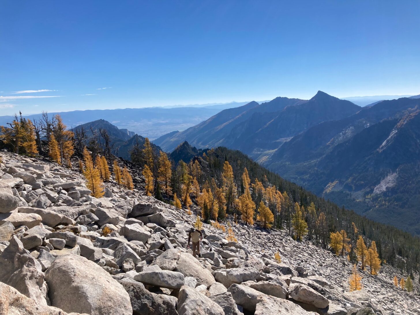 A hiker walks through a slope covered with boulders and mountains are in the background.