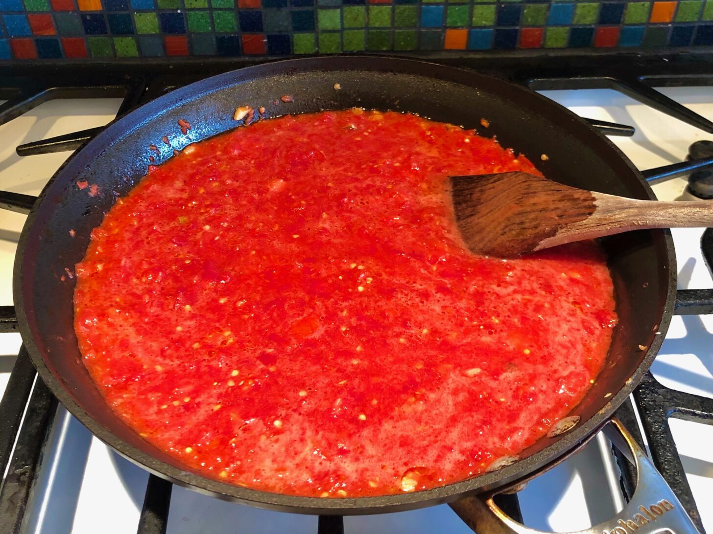 a pan of homemade tomato sauce simmers on a stove. A wooden spoon is sticking out of the sauce.