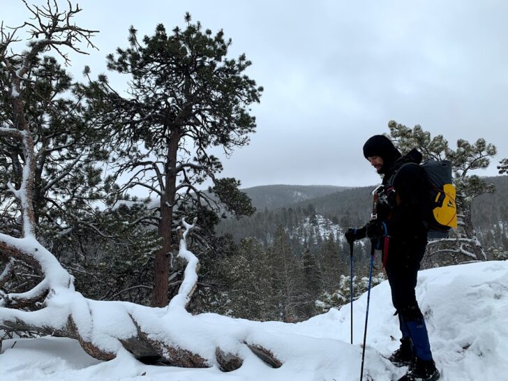 a man stands on a snowy cliff wearing a small backpack