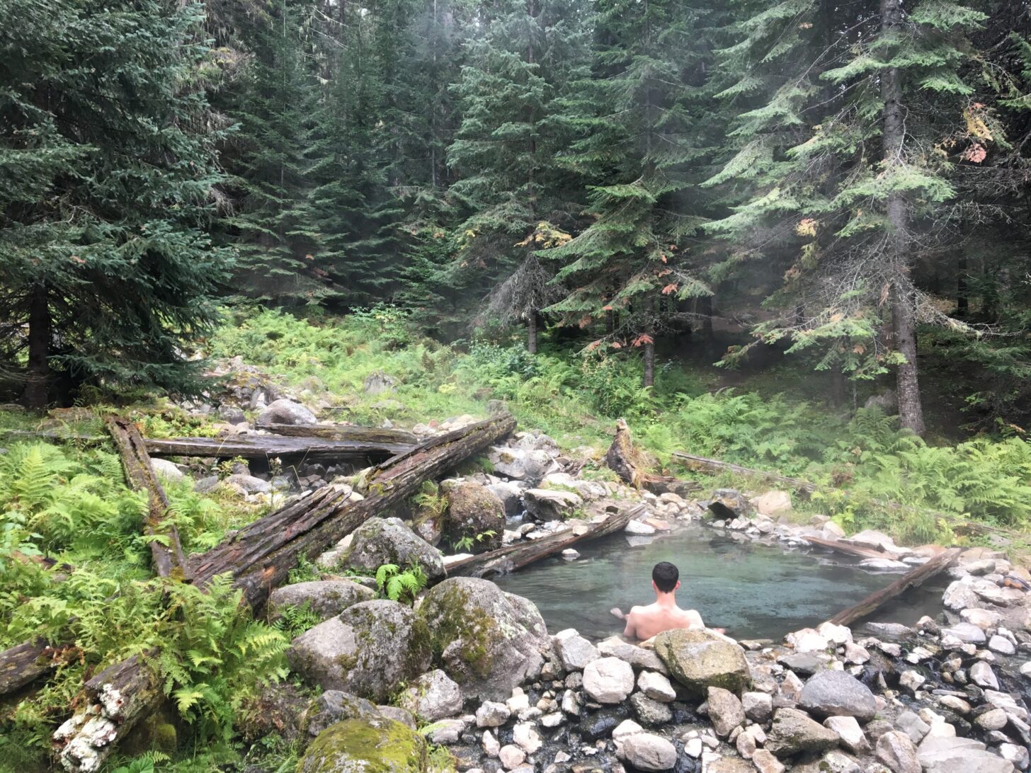 A man sits in a hot springs in a forest.