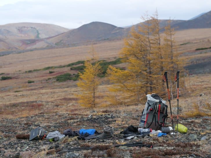 A backpack sits on the ground with mountains in the distance. Strewn about are various other supplies. Photo: Tully Henke