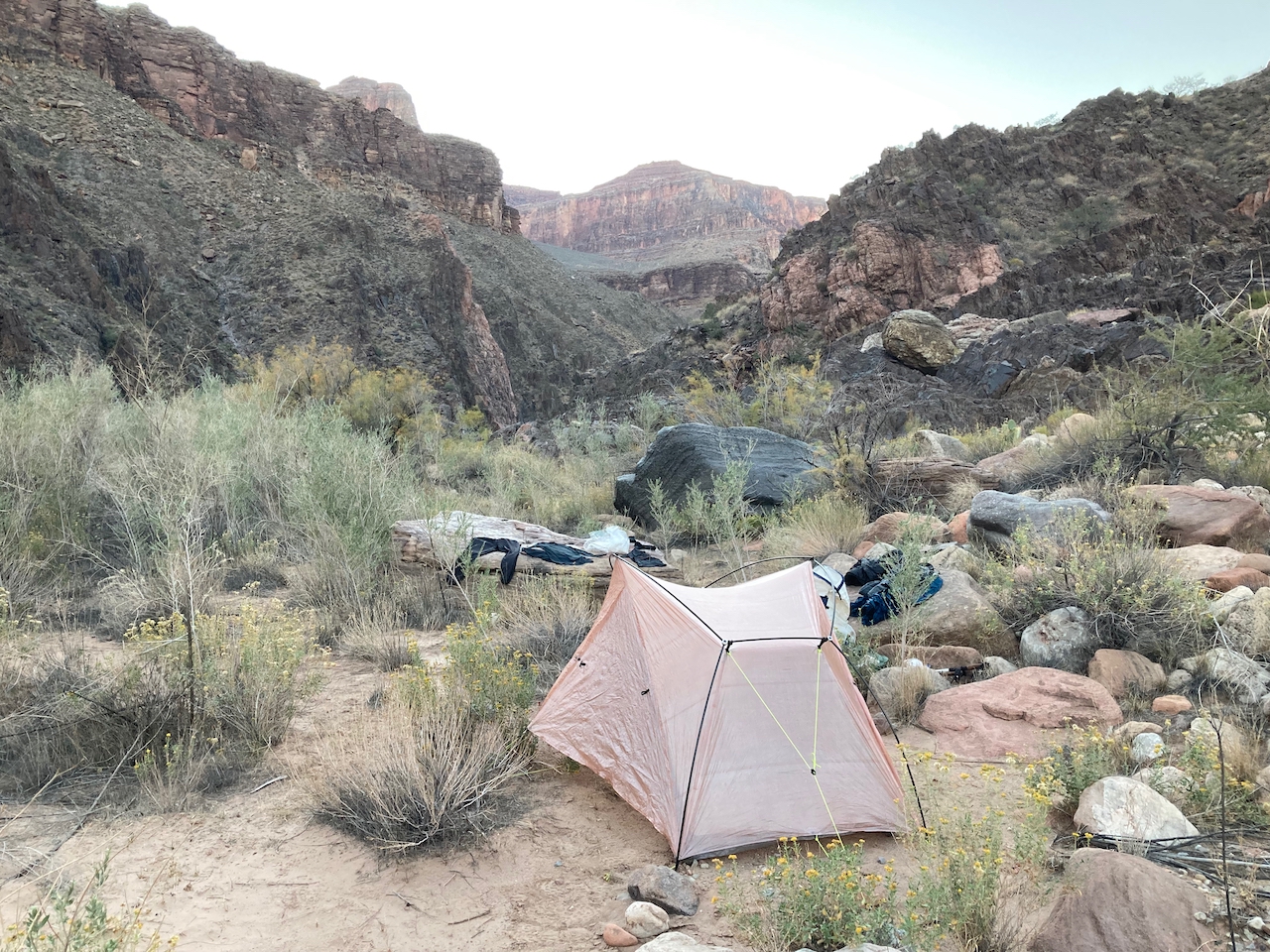 a wide shot of the zpacks free duo nestled in a campsite with canyon walls all around. The color of the shelter matches the colors in the rocks and sand all around the shelter.