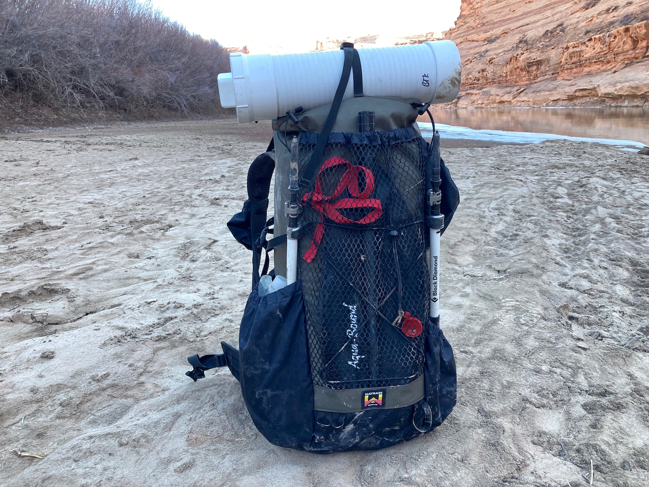 A medium shot of the waymark gear company Lite 50L on a riverbank, loaded down with gear.