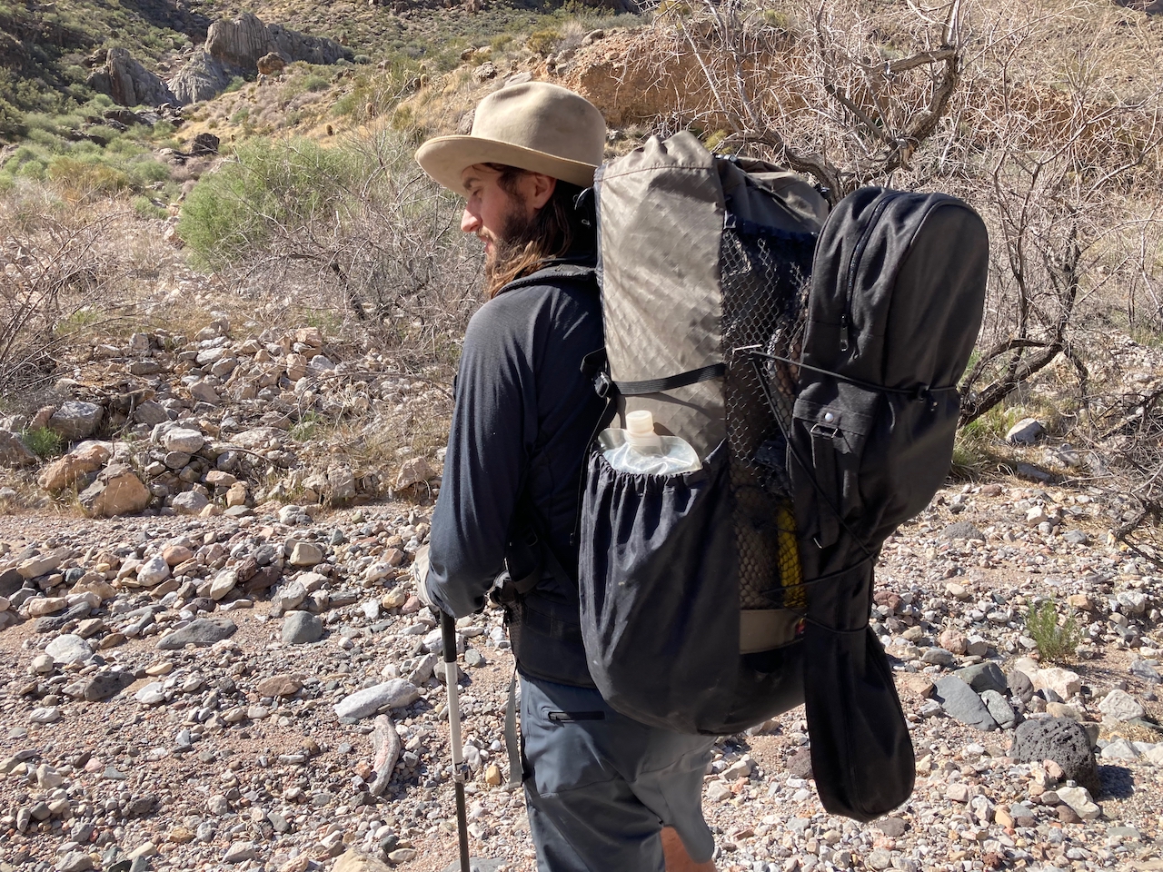 A man walks away from the camera while wearing the Waymark Gear Company Lite 50L loaded down with lots of water and a guitar.