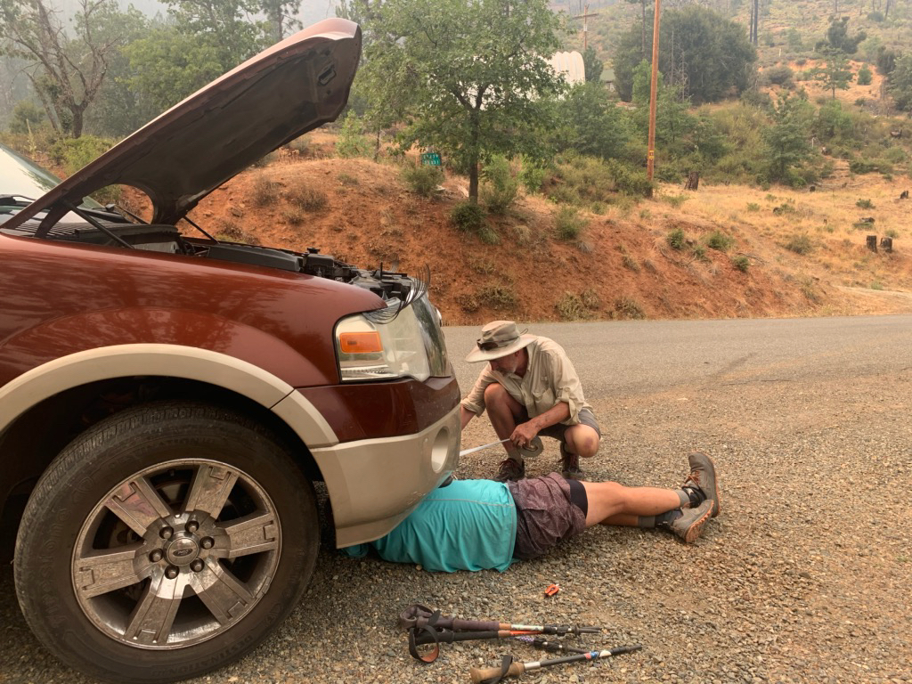 two men using ducktape to fix a hole in a radiator hose in a large vehicle.
