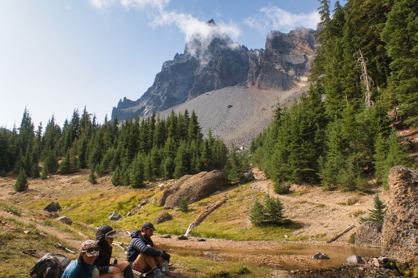 a group of hikers take a break below a rugged peak.
