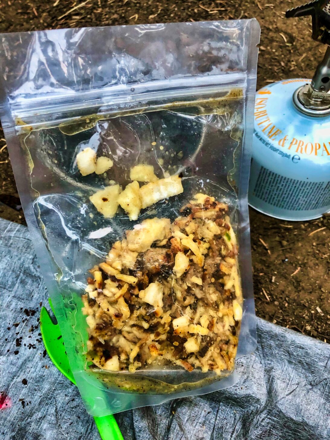 a bag of backpacking food with a spoon and a stove in the background.