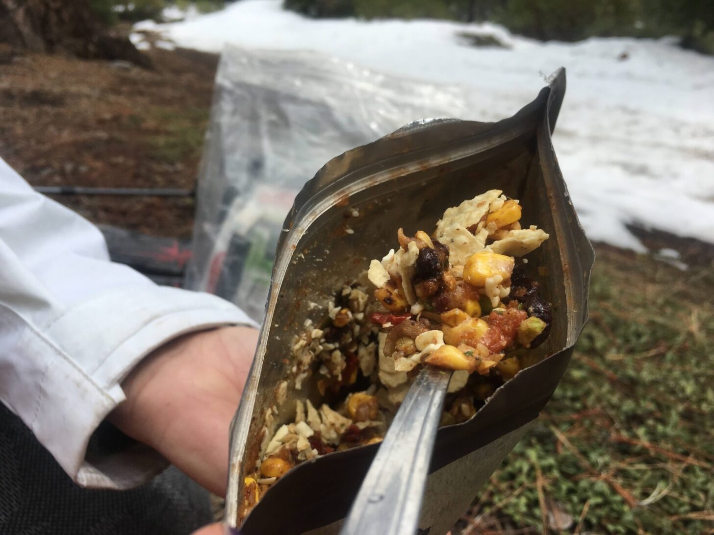 a hand holding a bag of backpacking food with a spoon sticking out of it.