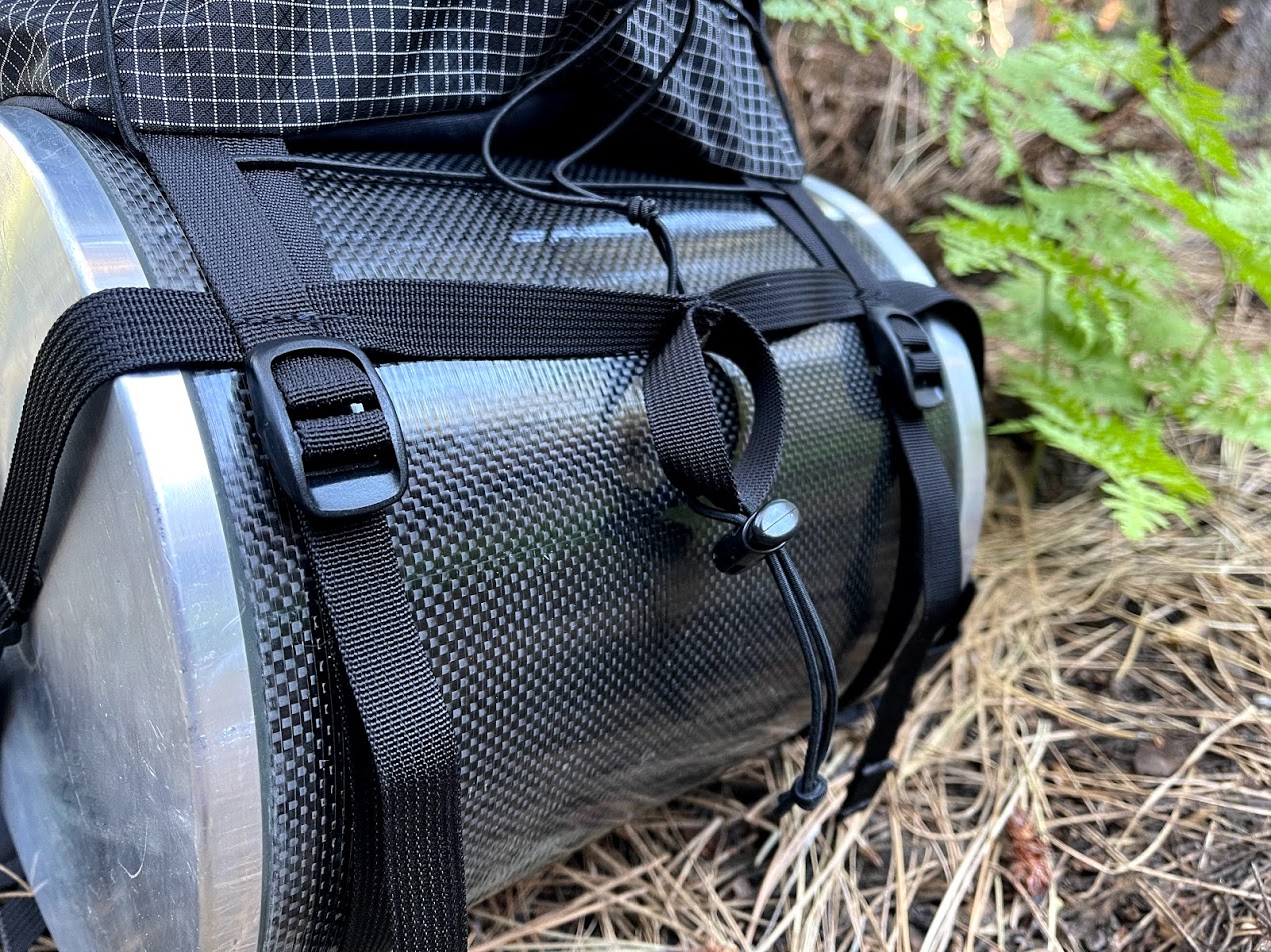 A close-up of a bear canister attached to a pack.