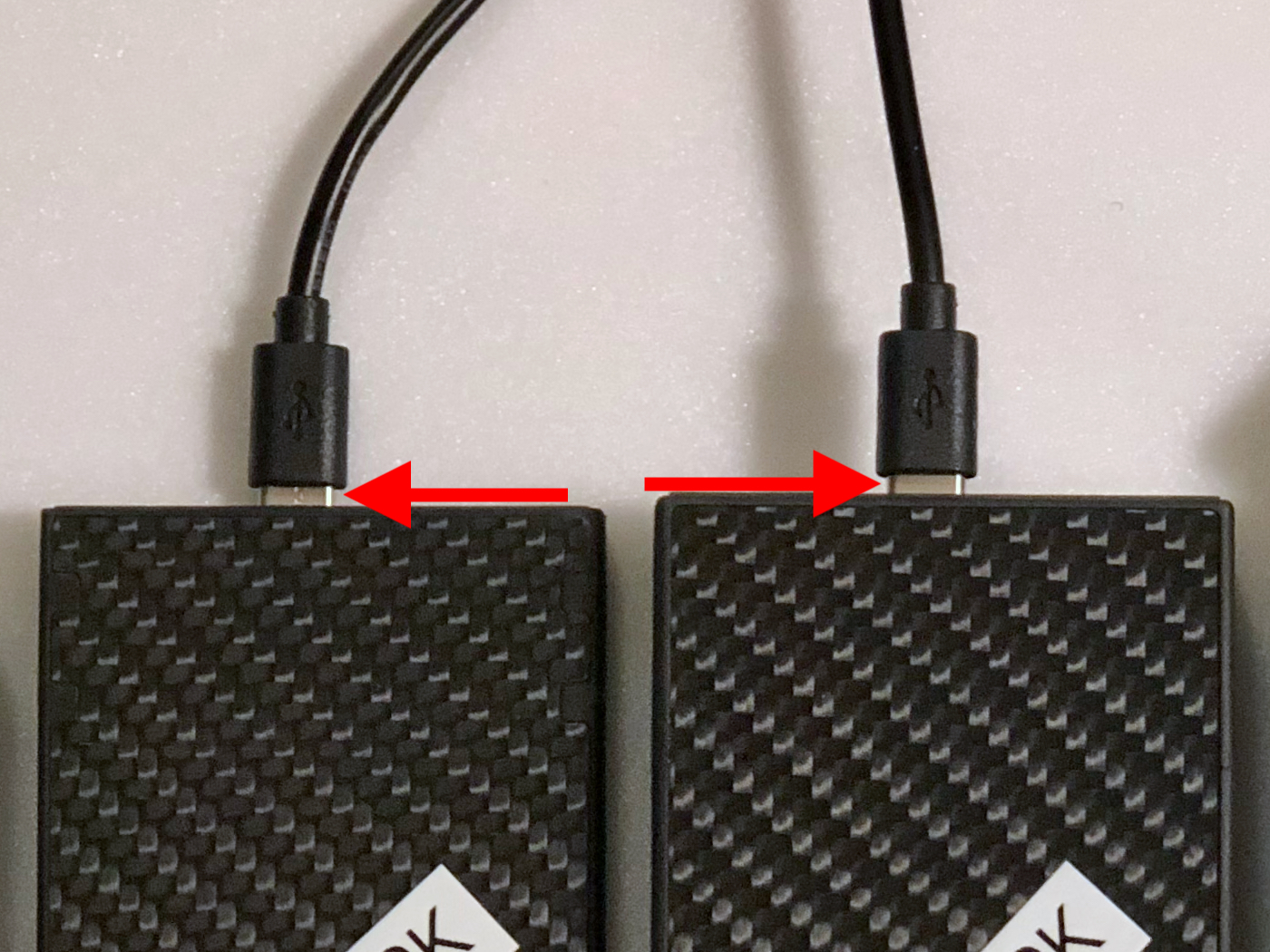 The Nitecore 10K (left) and Nitecore 20K PBCs with USB-C cables plugged in. Red arrows point to exposed connectors.