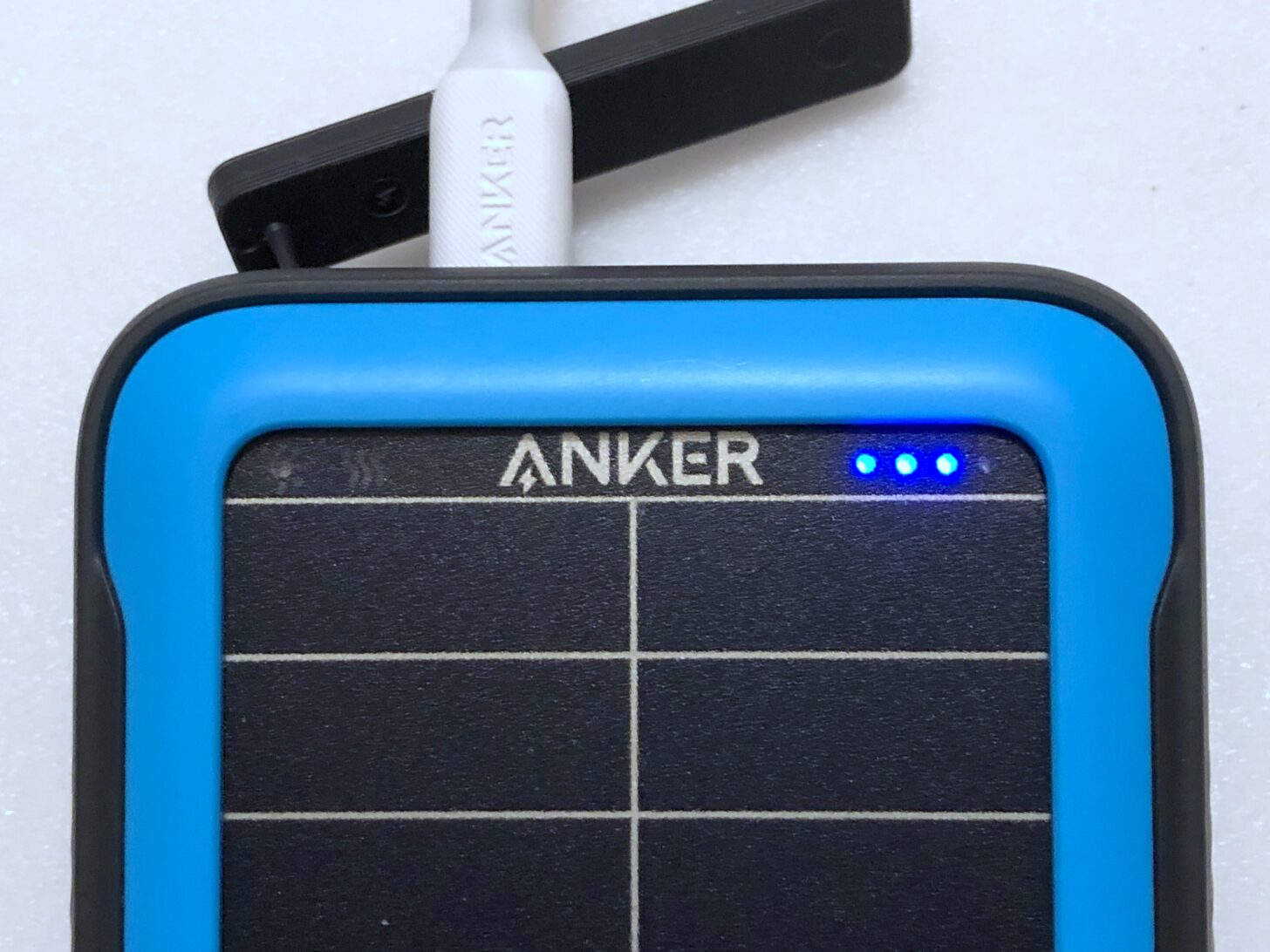 The Anker 20K Solar with three out of four indicator LEDs glowing and the port cover under a USB cable.