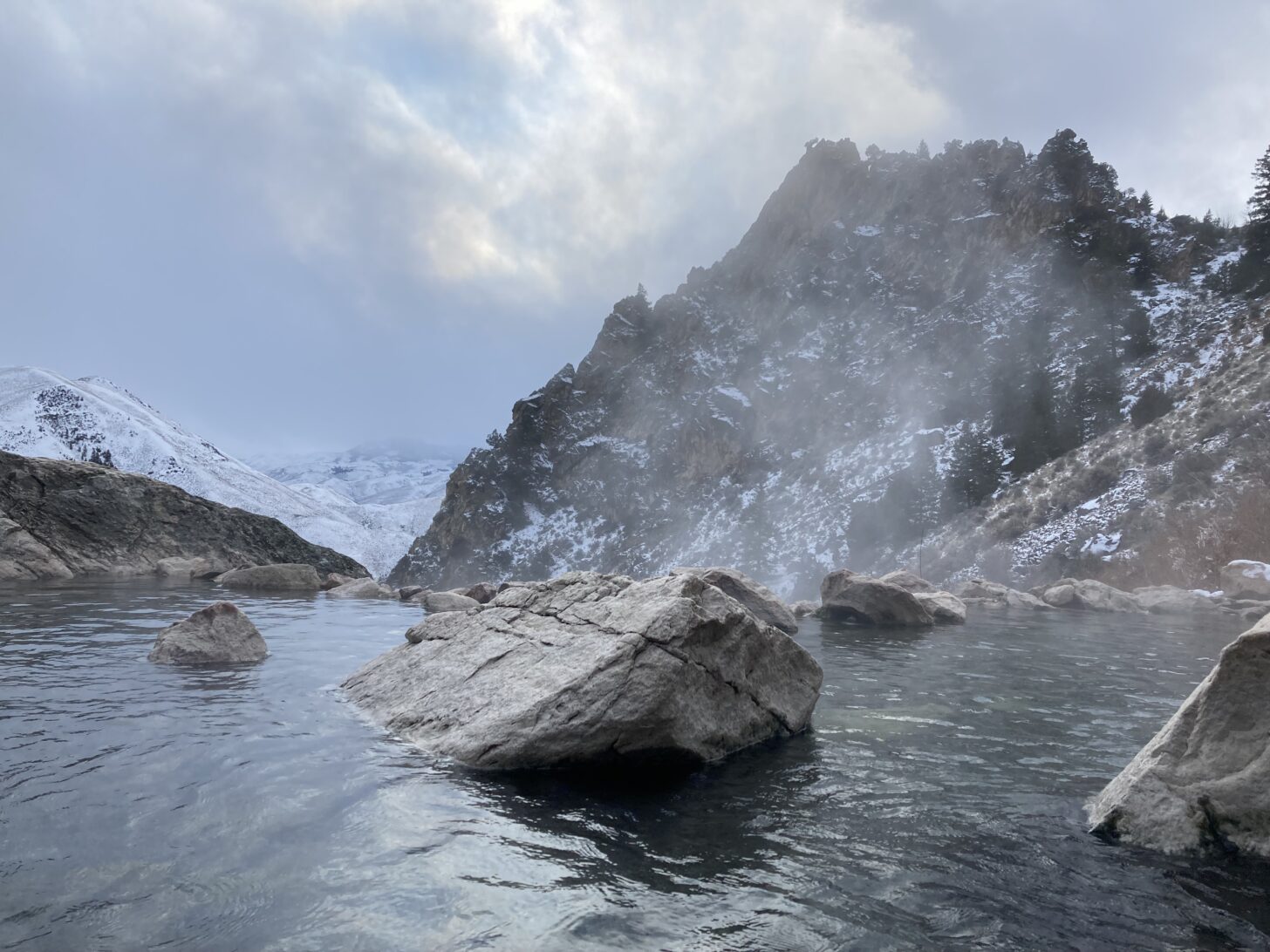 A hot springs in winter with a mountain in the background.